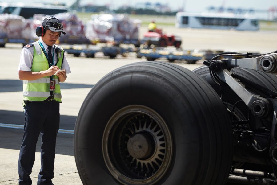 A man in a yellow vest standing next to an airplane tyre. 