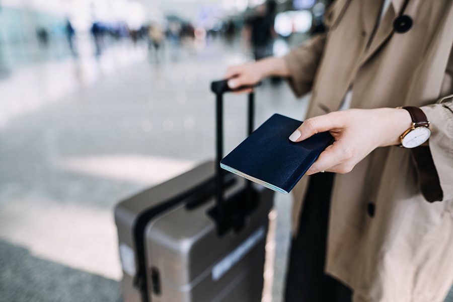 A traveller holding a passport and a suitcase at the airport.