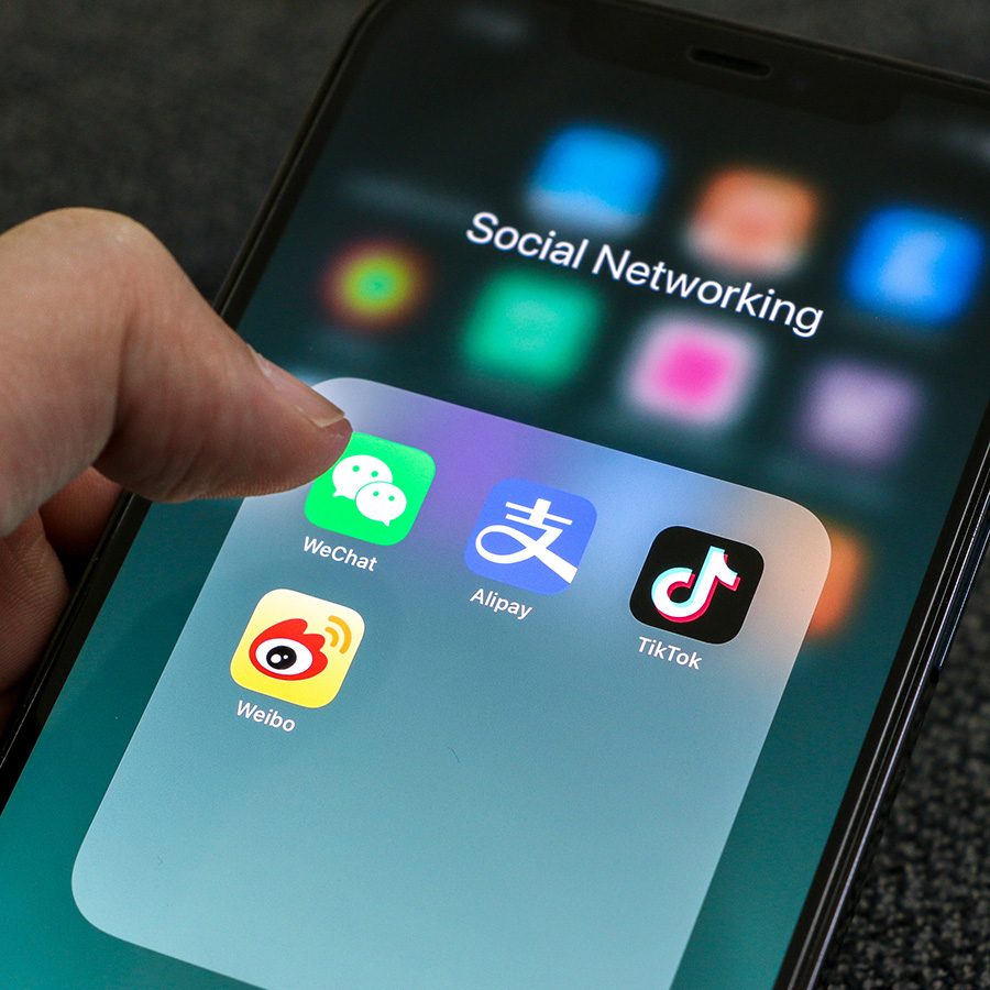 Close-up of a hand holding a smartphone. The screen shows icons for WeChat, Alipay, TikTok and Weibo.