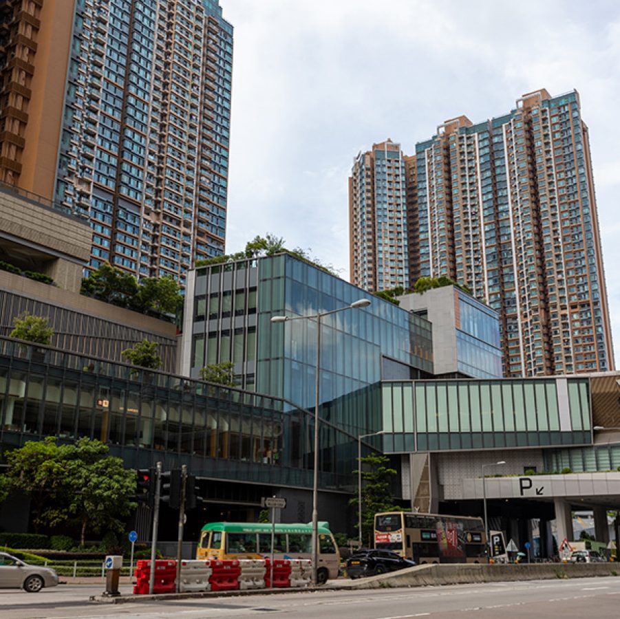 The façade of Yoho Mall, with residential buildings behind and cars and buses on the road in front. 