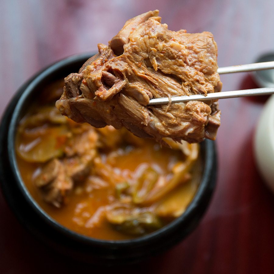 A closeup of a person holding up a piece of tender braised short rib over a bowl of galbijjim, served with a bowl of white rice