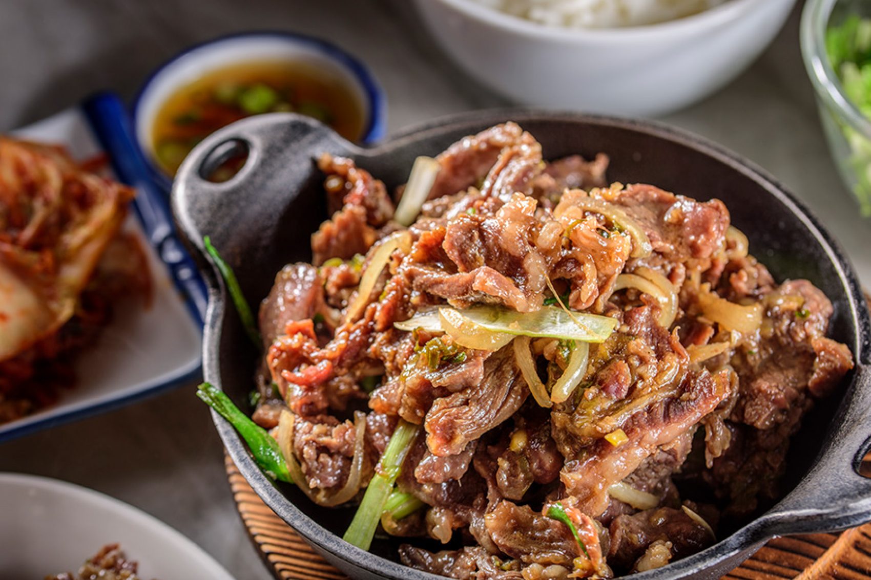 A closeup of a hot plate of beef bulgogi on a dining table laden with various Korean food