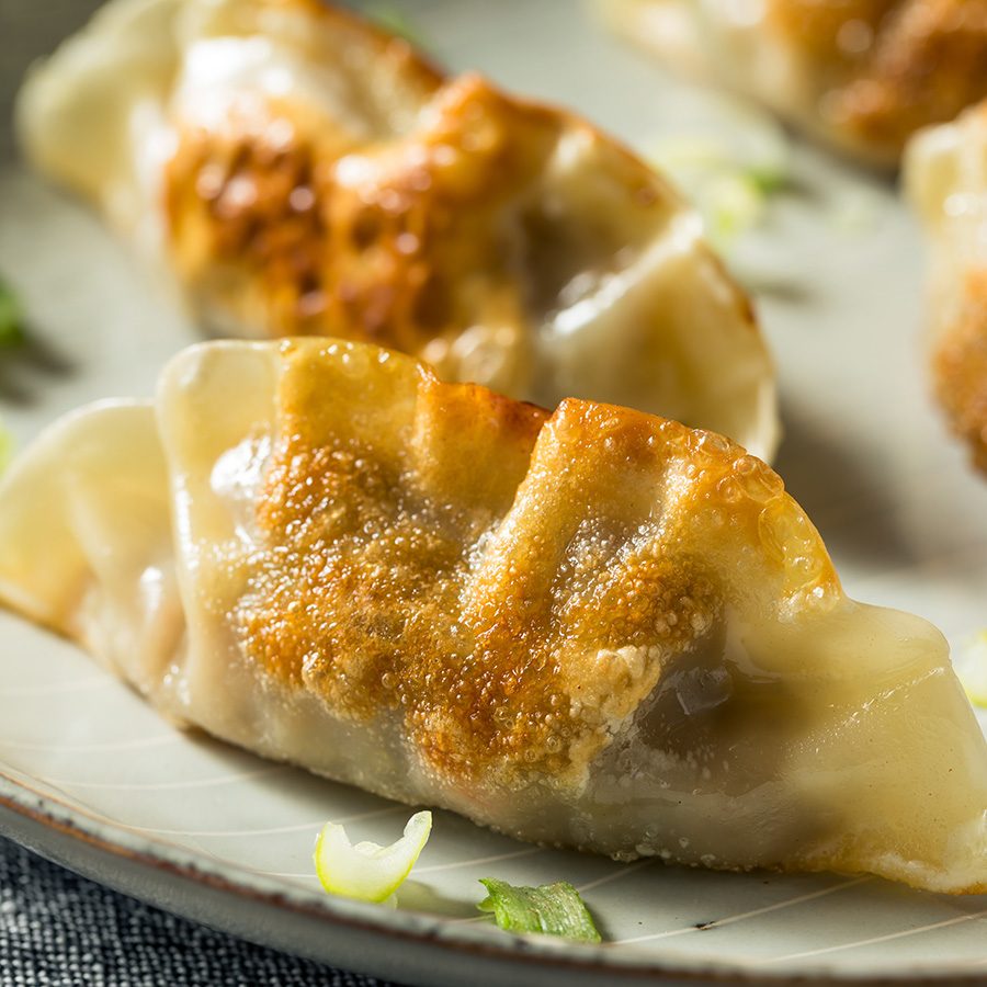 A closeup of a plate of fried mandu Korean dumplings garnished with scallion spring onions 