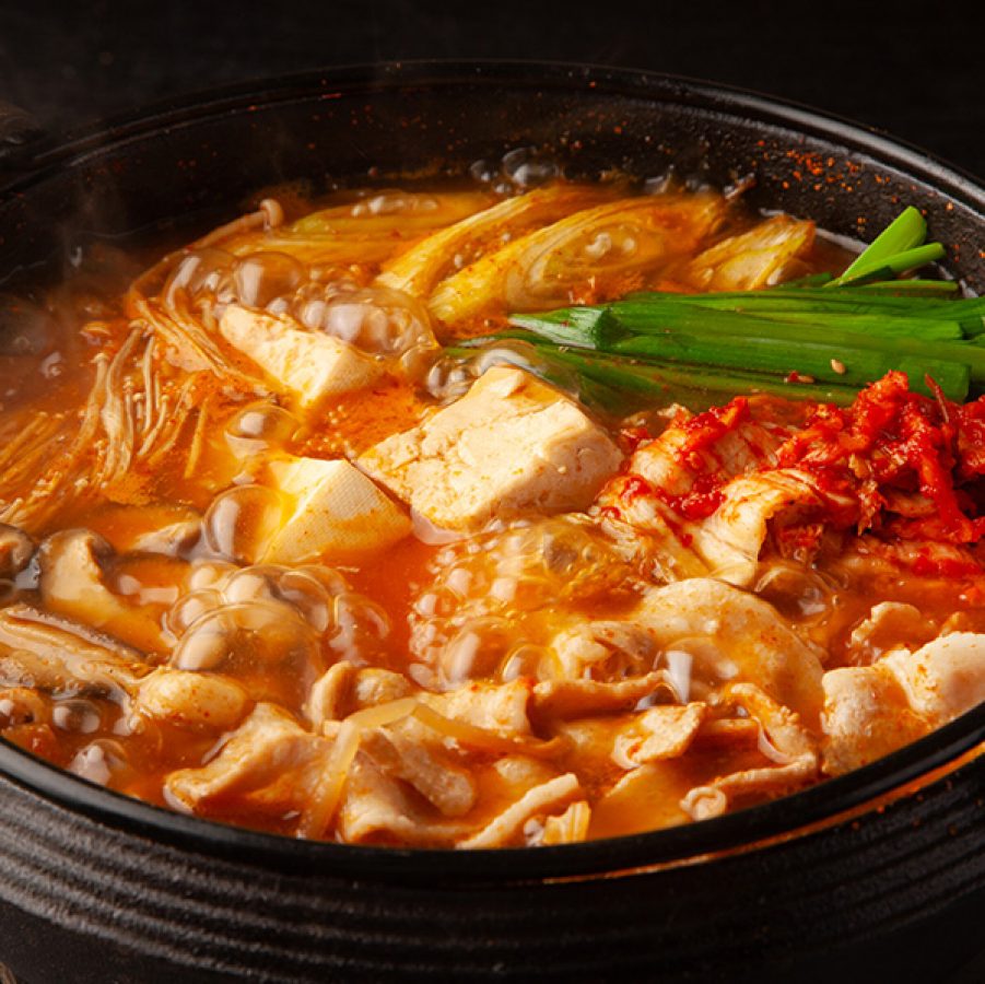 A closeup of a bowl of hot kimchi stew with mixed vegetables