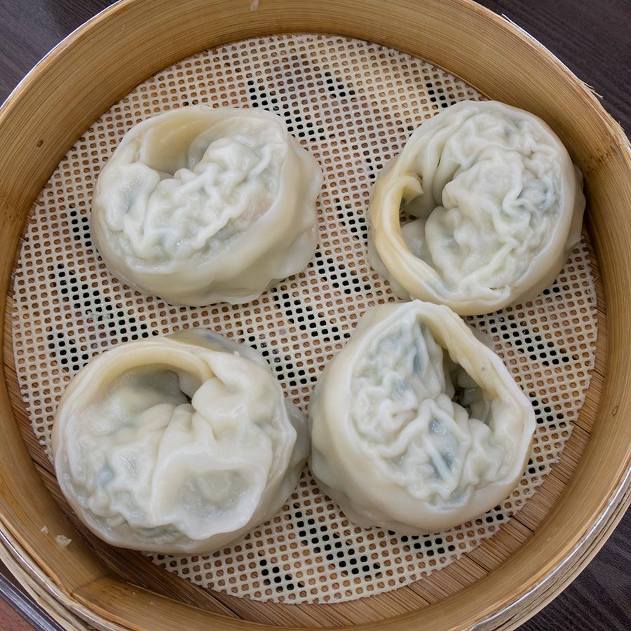 An aerial shot of four pieces of steamed mandu Korean dumplings in a bamboo steamer basket  