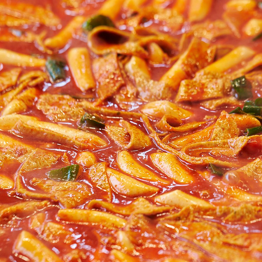A closeup of a large pan filled with steaming hot tteokbokki, Korean spicy stir-fried rice cakes 