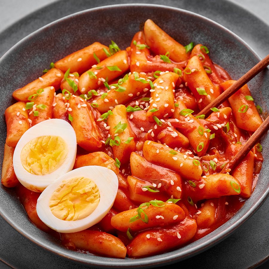 A closeup of chopsticks picking from a plate of tteokbokki with sliced boild egg 