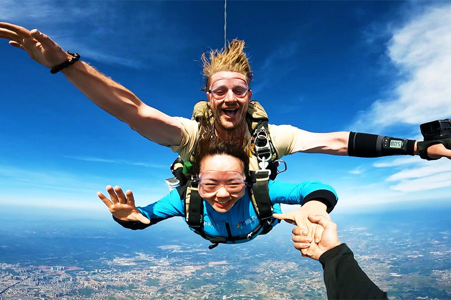 A man and a woman look excited as they skydive and pose for a photographer who captures the moment. 