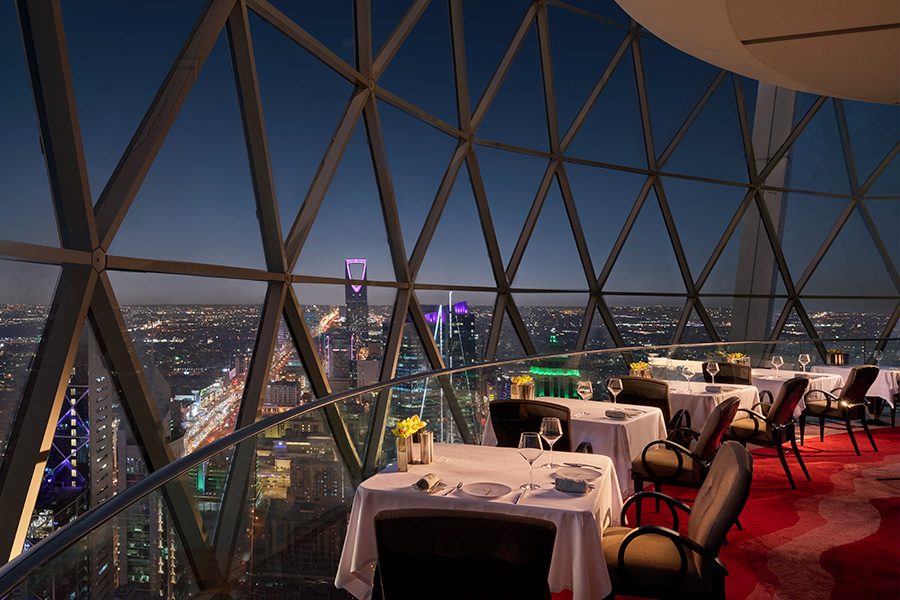 Dining tables lined up alongside the windows of The Globe with views of Riyadh below.