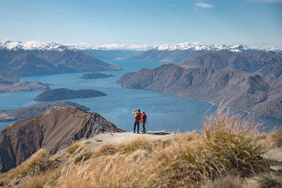 Two people standing at a vista point with views of a lake and mountains in New Zealand