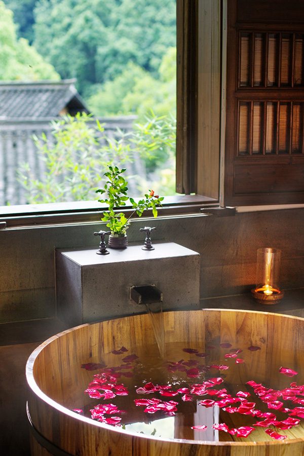 A serene view of a wooden bath filled with rose petals next to a window at Amanfayun in Hangzhou, China 