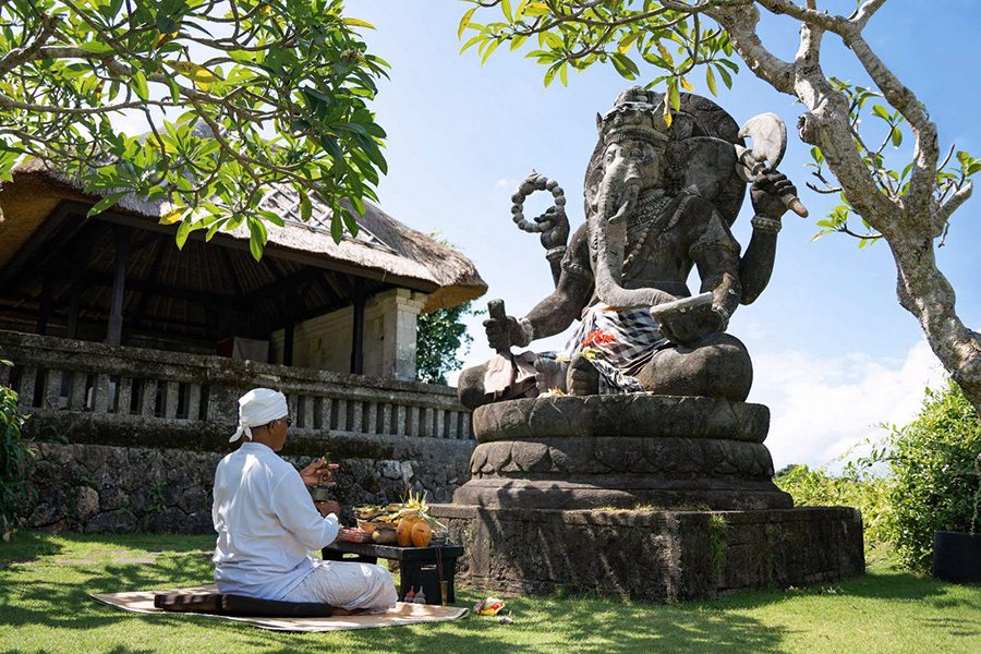 A man meditates in front of a Balinese elephant god statue during the day at the Bulgari Resort Bali temple 