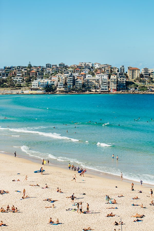 People on a beach in Sydney. Buildings can be seen at the other end of the bay