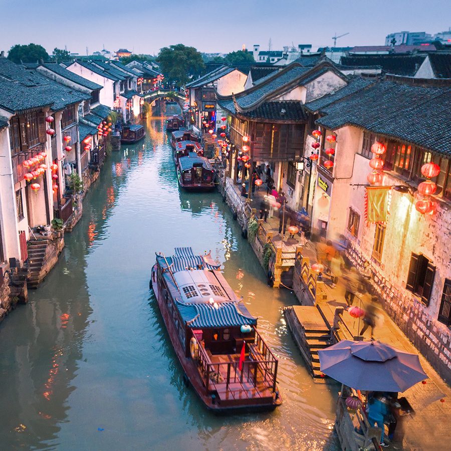 A boat floating across a canal in Suzhou, lit up in the evening.
