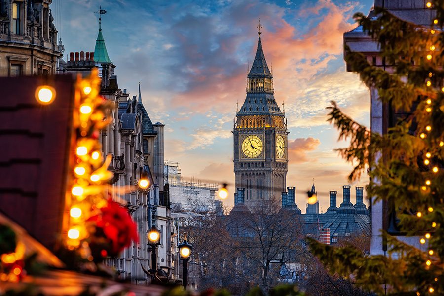 London’s Big Ben appears from behind a brightly lit Christmas stall and Christmas tree, just before sunset 