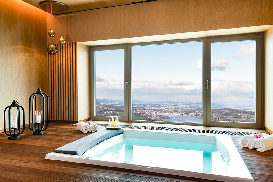 A spa room at Bürgenstock Hotel & Alpine Spa, featuring a thermal bath and a window with a view of the Lucerne