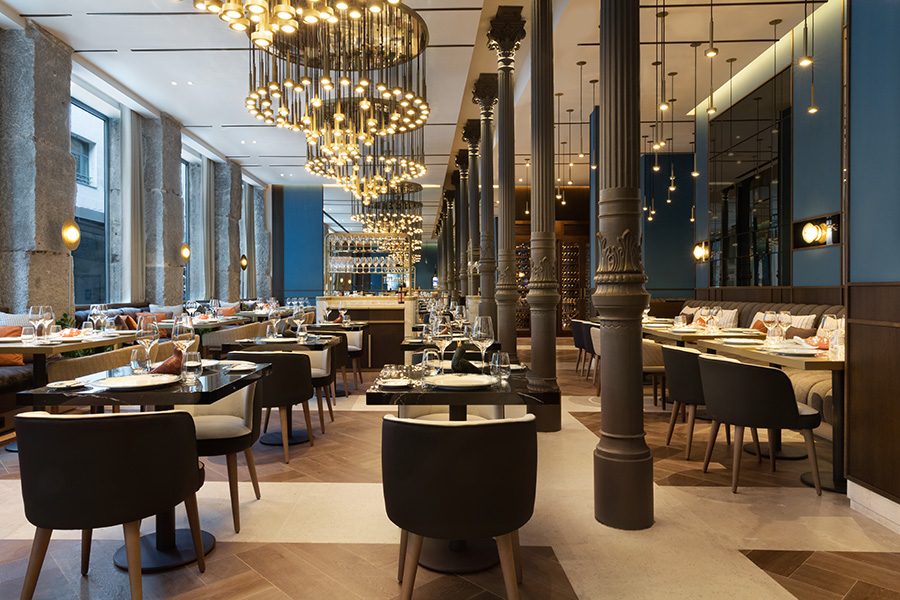 Rows of tables line a restaurant with blue walls, floor-to-ceiling windows and pendant lights at JW Marriott Hotel Madrid 