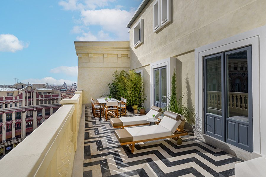 A stylish sunlit terrace on the top floor of a cream-coloured building, looking out onto the centre of Madrid