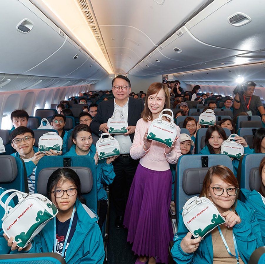 Interior shot of a Cathay Pacific Community flight and people holding up Cathay Pacific-branded bags.