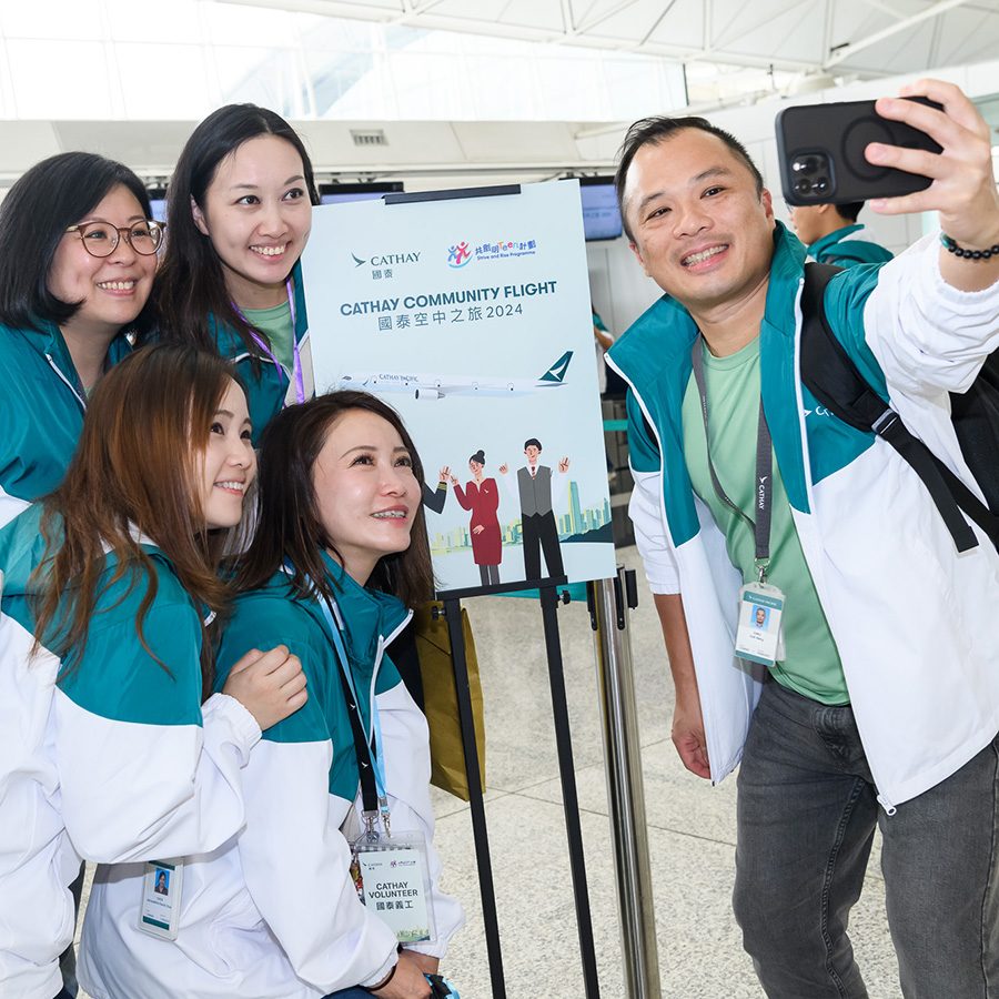 Man takes a selfie by a Cathay Pacific Community Flight sign alongside fellow passengers at the airport