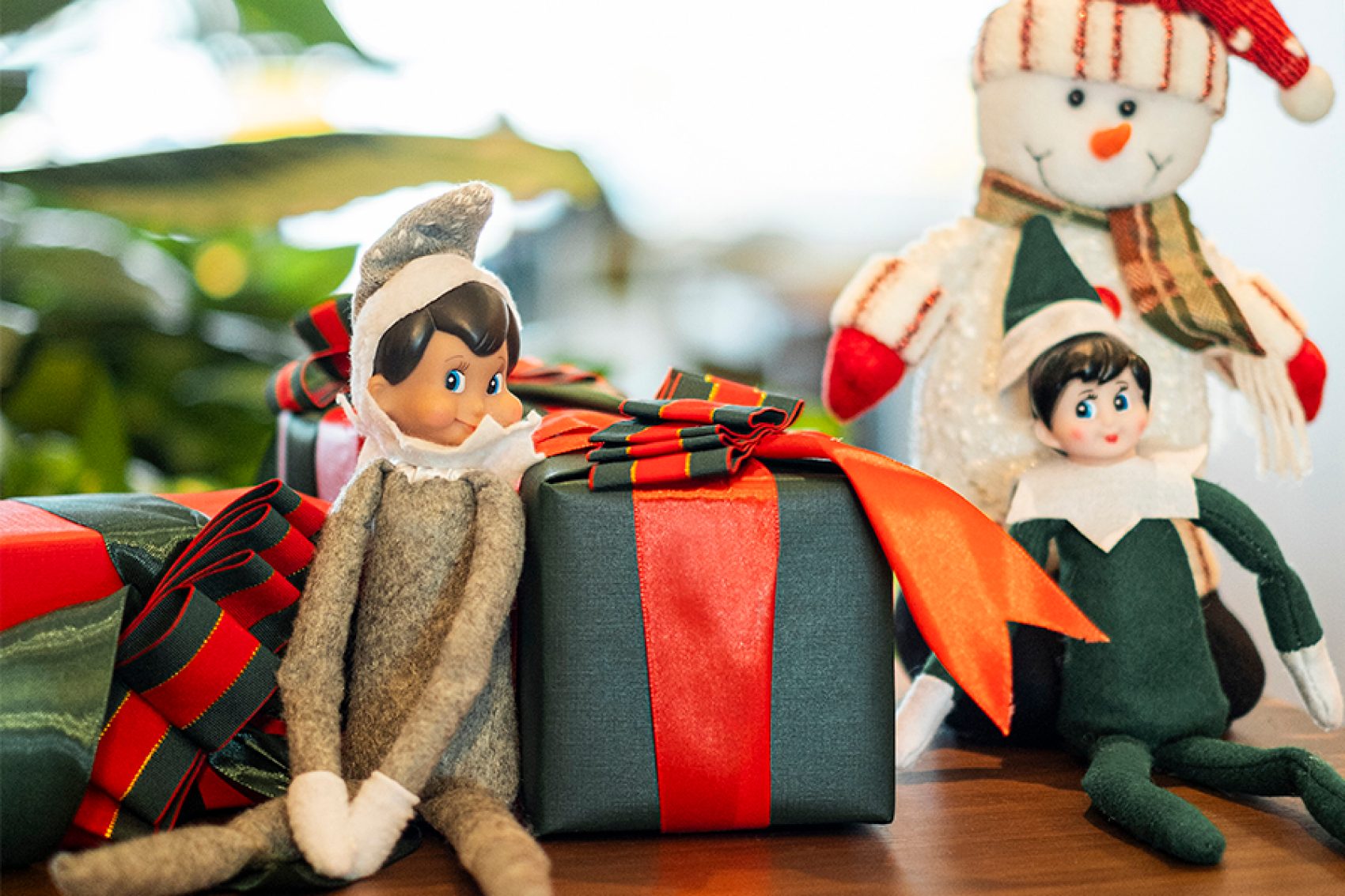 Two Elf on the Shelf toys placed next to small gift boxes and a snowman.