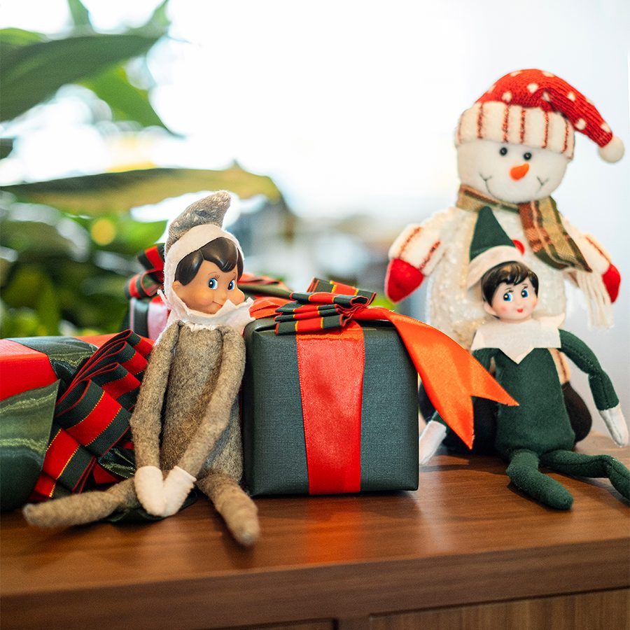 Two Elf on the Shelf toys placed next to small gift boxes and a snowman.