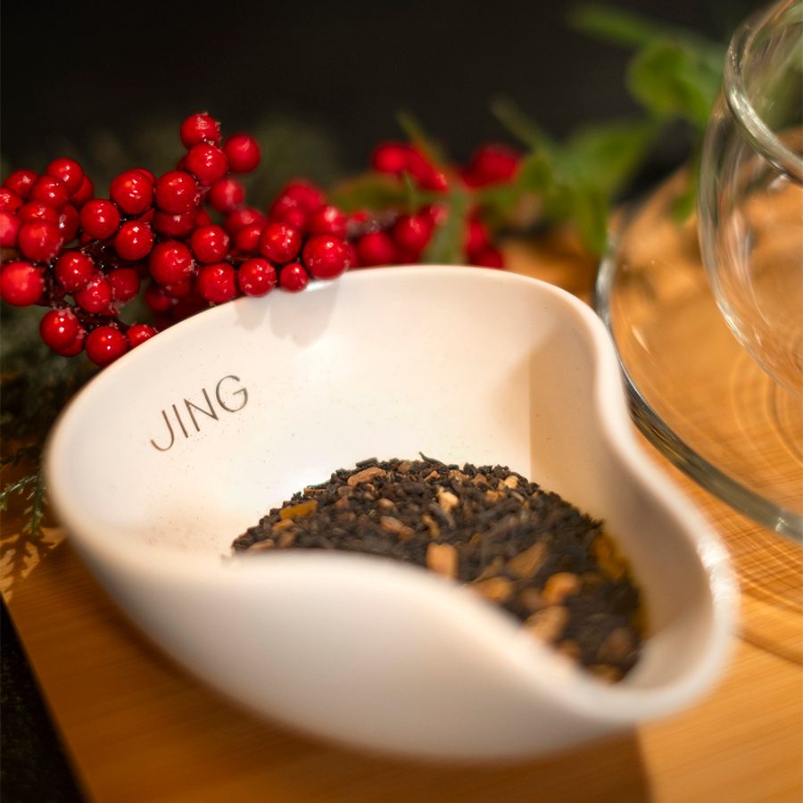 Close-up of a bowl of JING tea leaves with red berries behind it. 