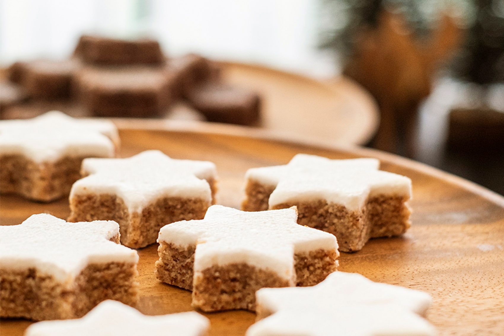 Close-up of Christmas cookies on a wooden plate with Christmas trees in the background.