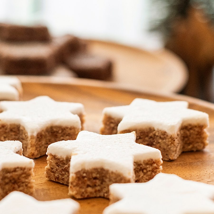 Close-up of Christmas cookies on a wooden plate with Christmas trees in the background.