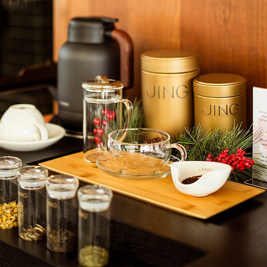 A table with JING tea caddies, teacups, a black kettle, glass tubes and a wooden tray.