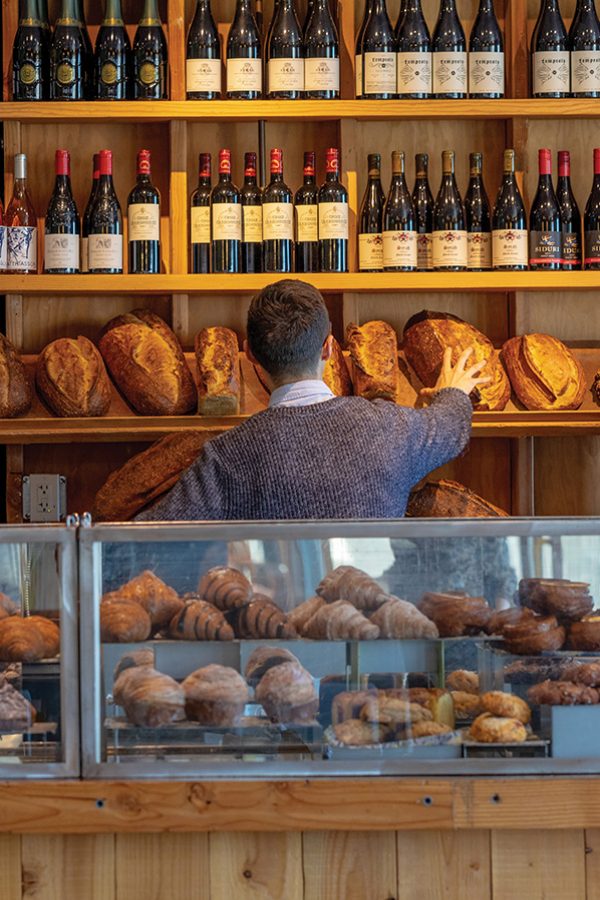 Man in a bakery with shelves of wine above him