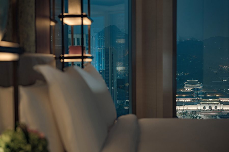 A bed next to a window in Four Seasons Hotel Seoul with a nighttime city view.