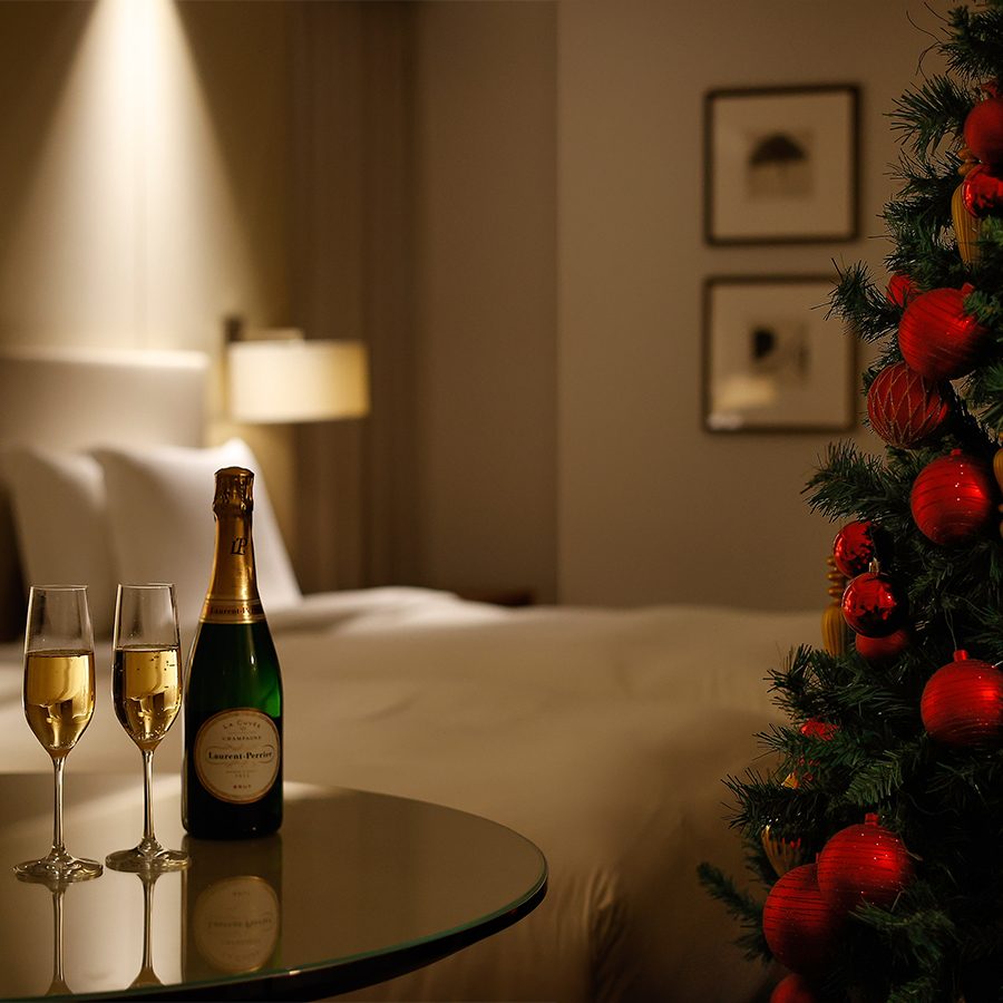 A bottle of champagne and two glasses on a table next to a Christmas tree in one of Palace Hotel's bedrooms.