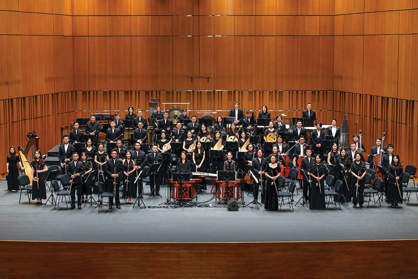 Members of an orchestra dressed in all black are holding their instruments while standing on stage.