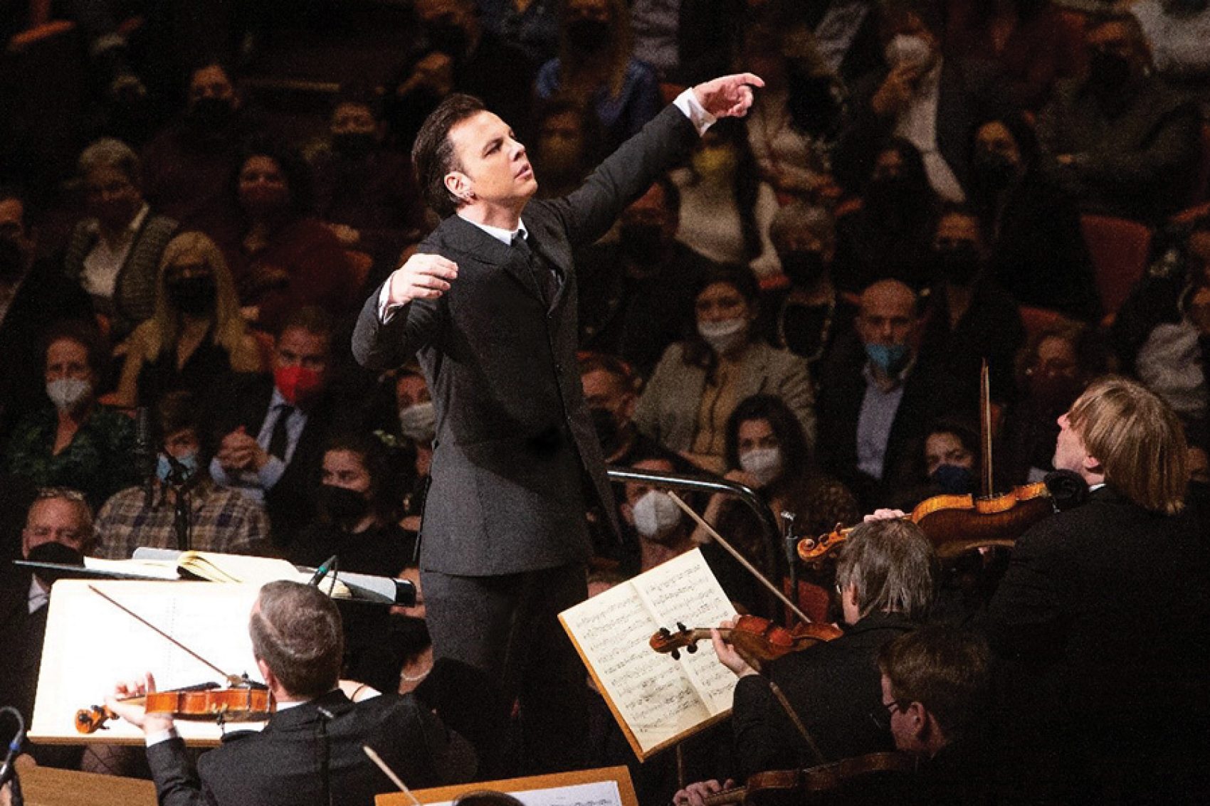 Conductor Teodor Currentzis on stage in a suit with Russian ensemble MusicAeterna Orchestra in front of him and the audience behind.