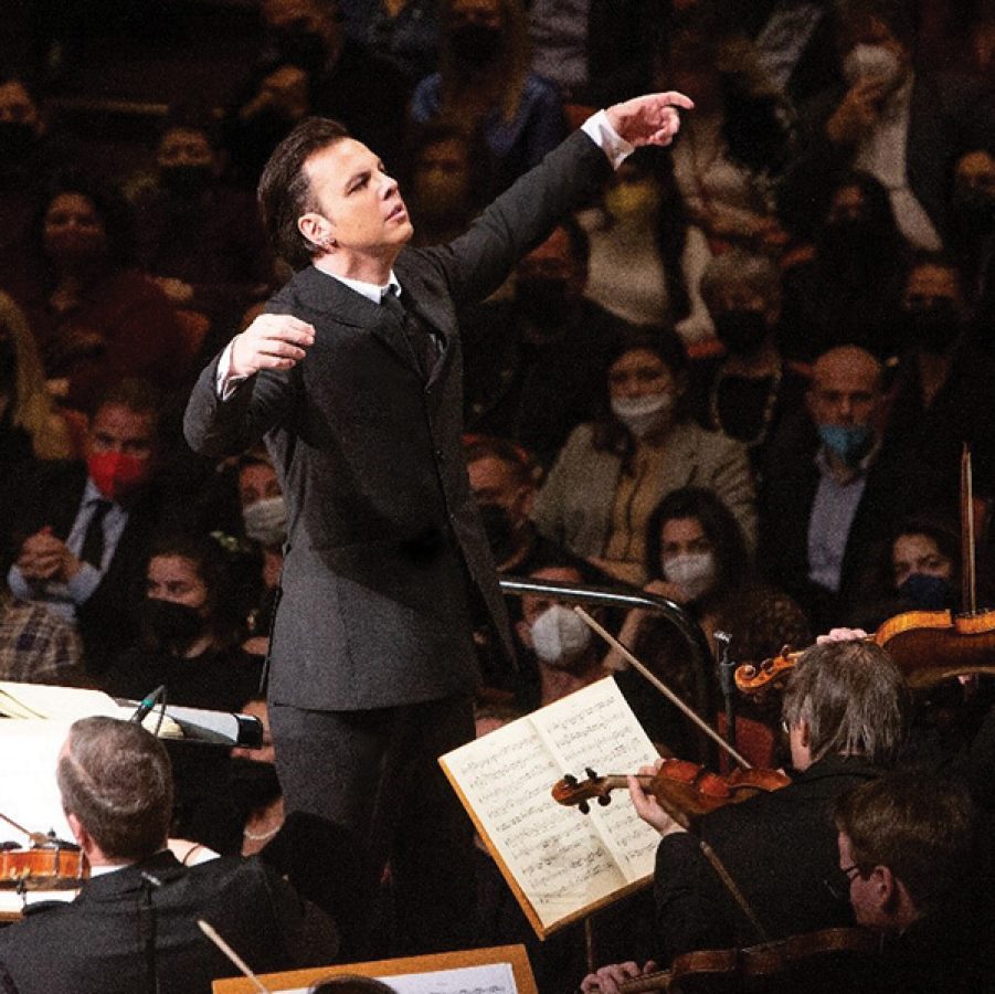 Conductor Teodor Currentzis on stage in a suit with Russian ensemble MusicAeterna Orchestra in front of him and the audience behind.