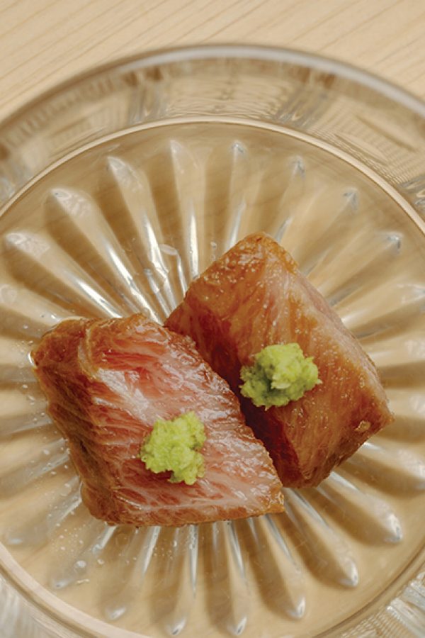 Close-up of smoked fatty tuna sushi topped with wasabi on a clear plate.