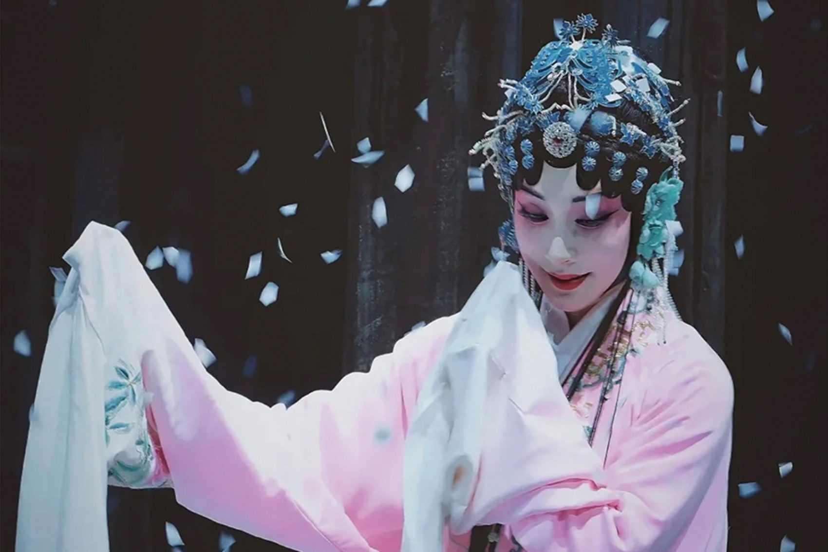 A woman in Chinese opera costume on stage with confetti around her.  