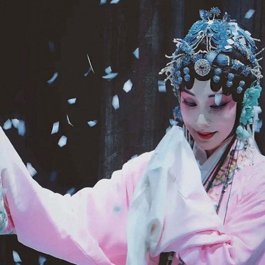 A woman in Chinese opera costume on stage with confetti around her.  