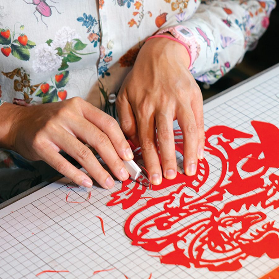 Nick Tsao cutting a Chinese-inspired design from red paper.