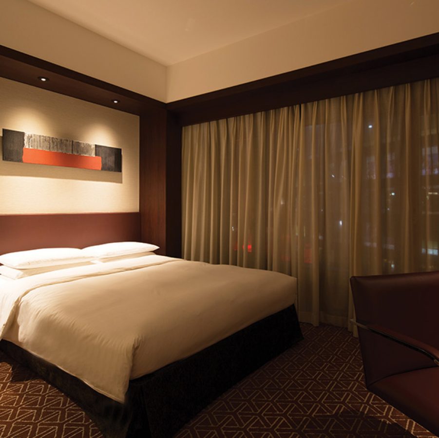 A softly lit guestroom decorated in neutral colours, featuring a large bed, window and desk chair, at Grand Hyatt Fukuoka 