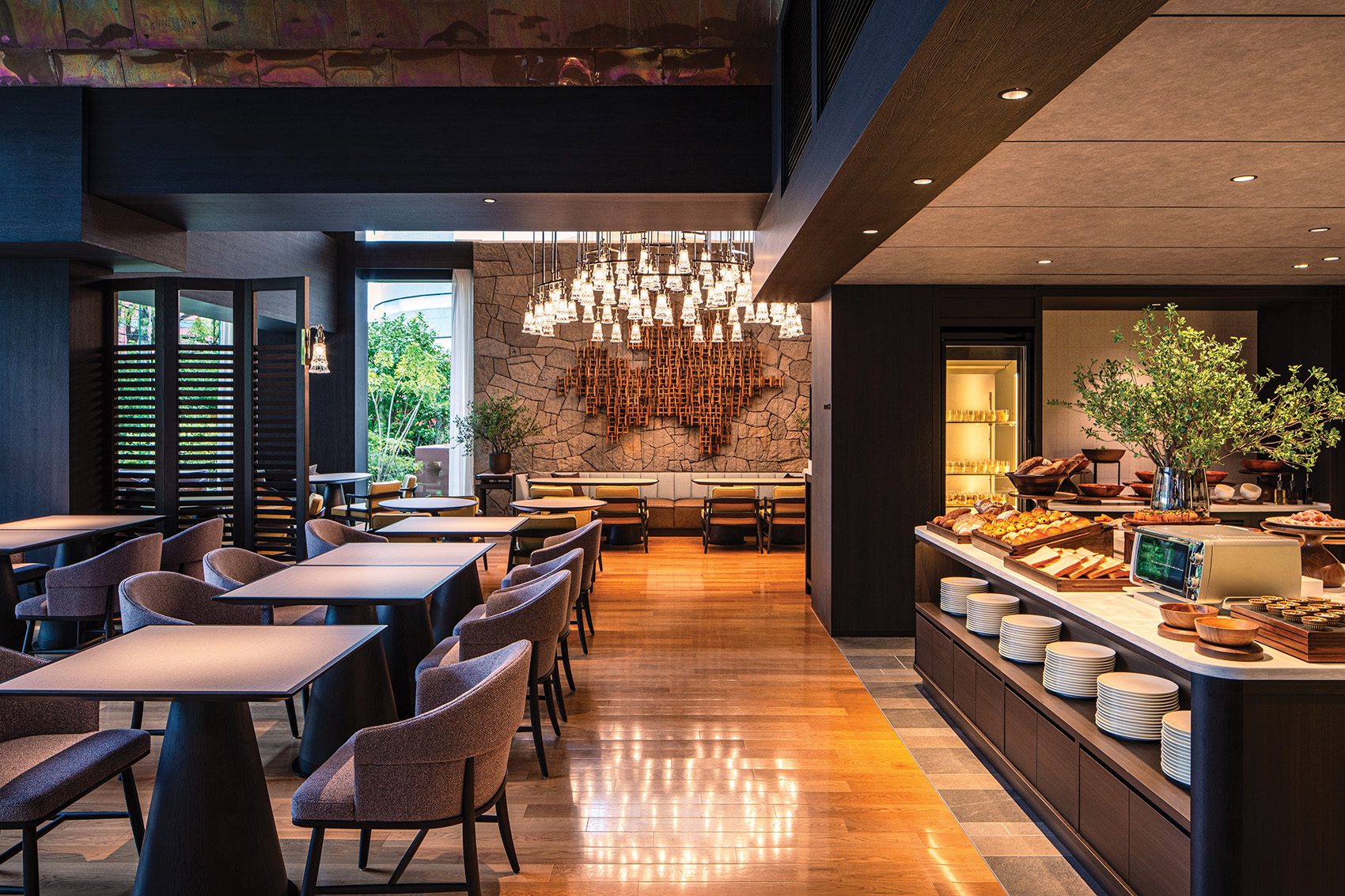 A spacious dining room decorated in neutral tones, with rows of tables and chairs and a buffet counter laden with food, at Grand Hyatt Fukuoka 