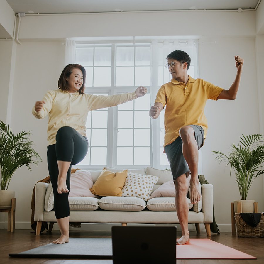 A man and a woman exercising on yoga mats in the living room.