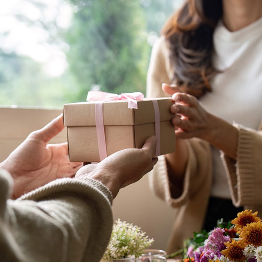 Close-up of a woman handing a gift box to another person.