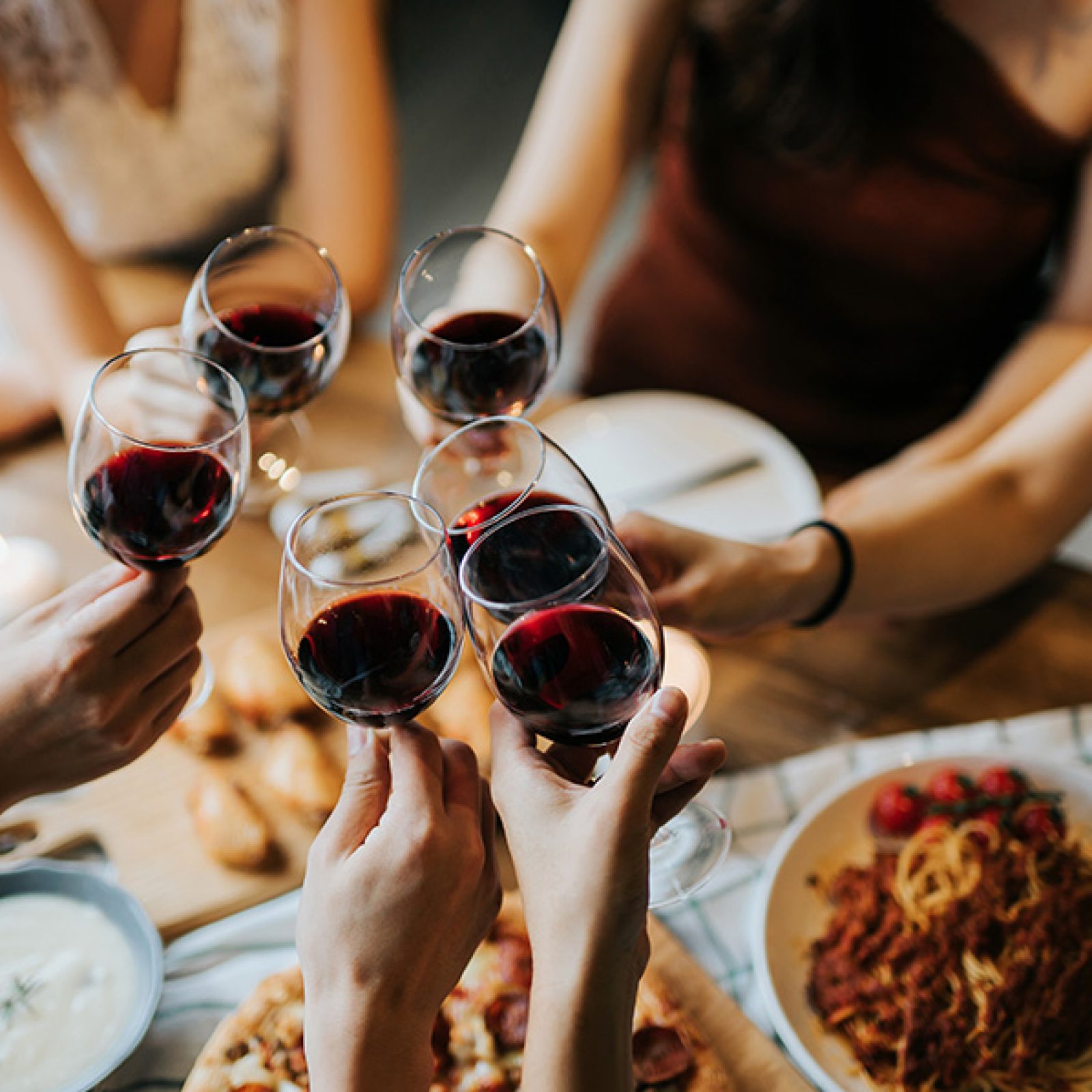 A group of people holding their wine glasses together over a table of food. 