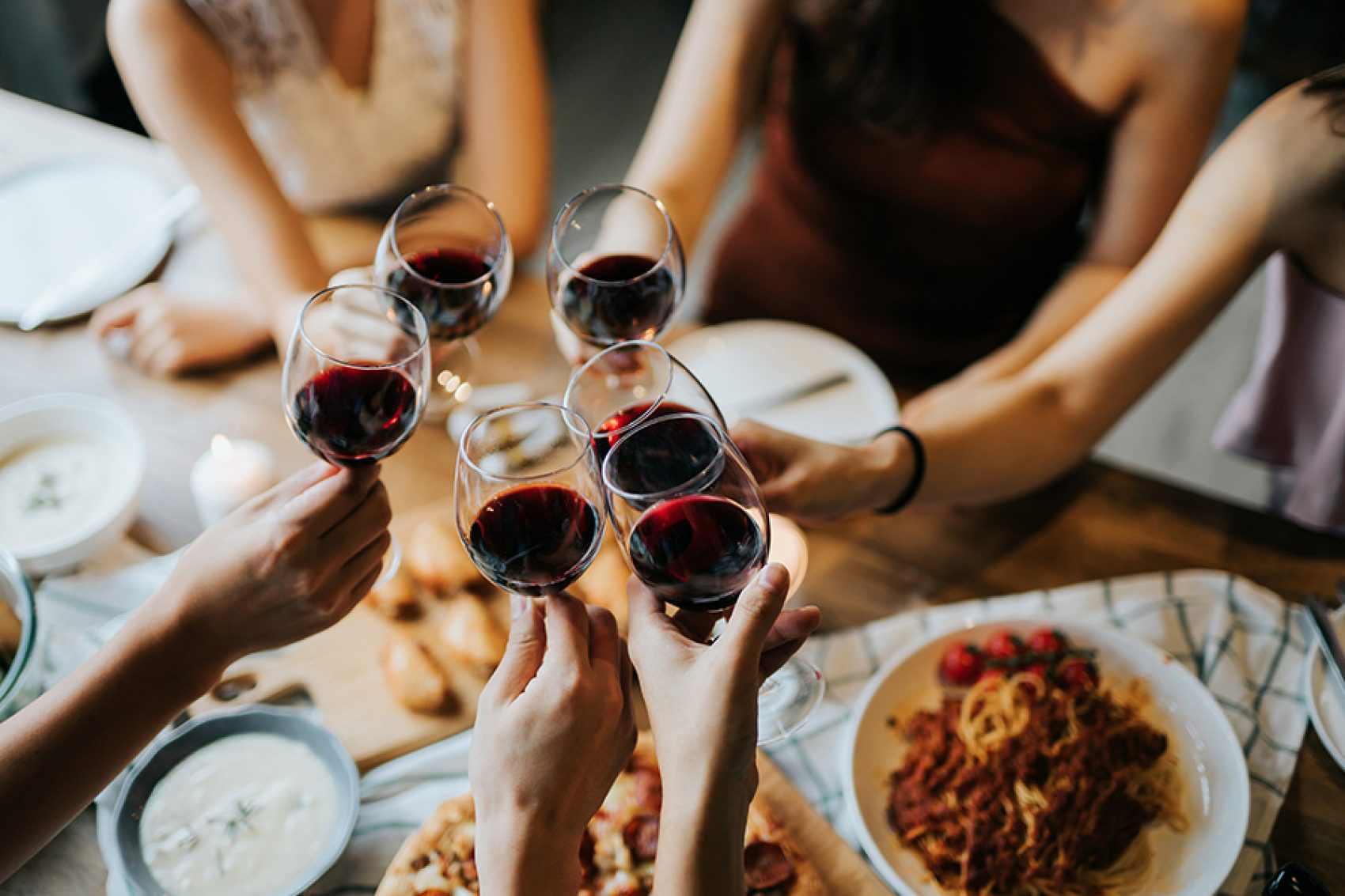 A group of people holding their wine glasses together over a table of food. 