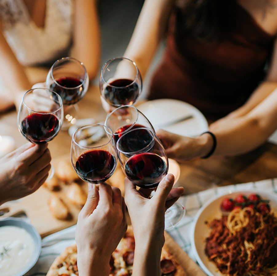 A group of people holding their wine glasses together over a table of food. 