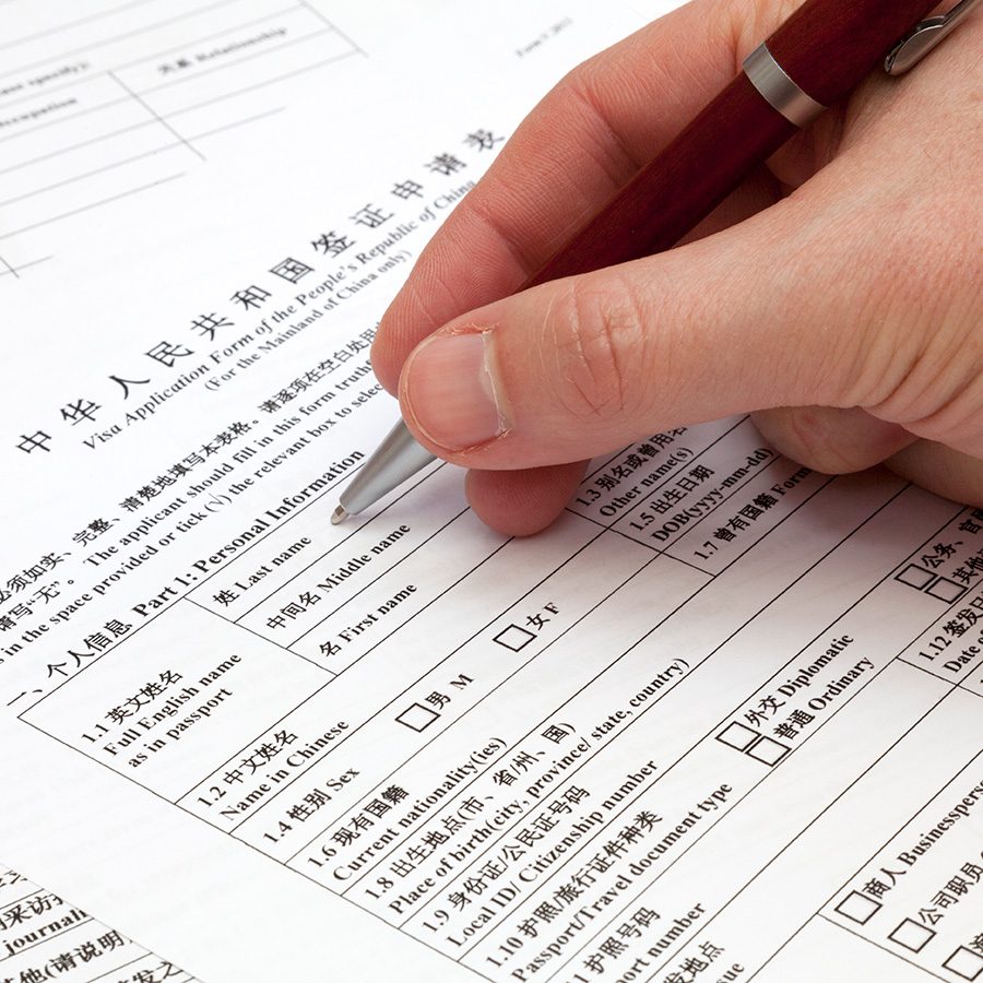 A hand holding a pen, filling out an application form for a Chinese visa.  