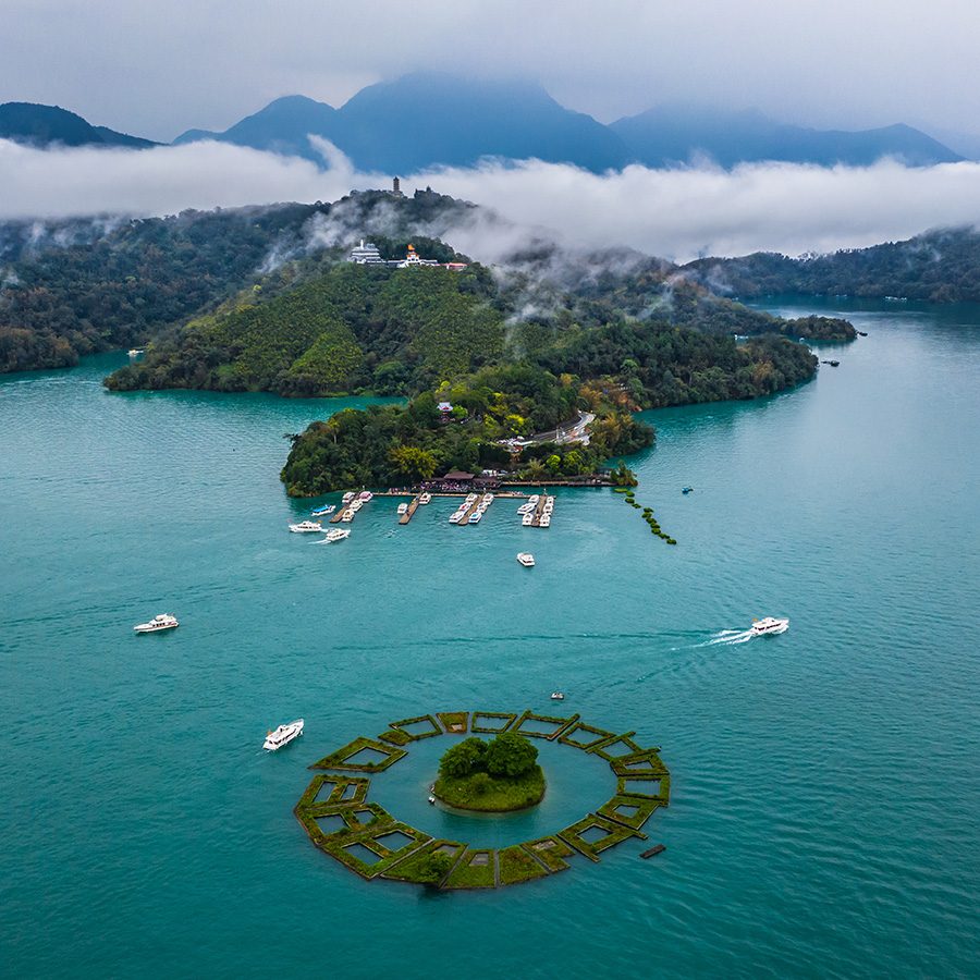 Sun Moon Lake from above, bordered by green mountains and low-lying clouds. 