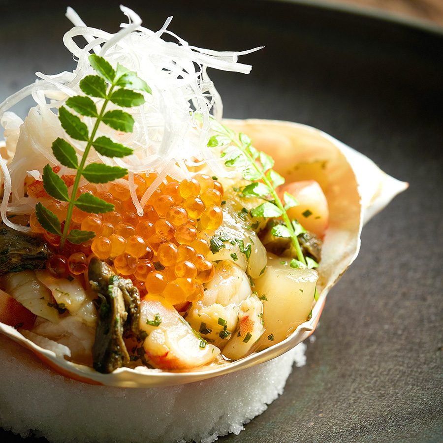A closeup of a dish with assorted seafood inside a crab shell at Inflorescence.